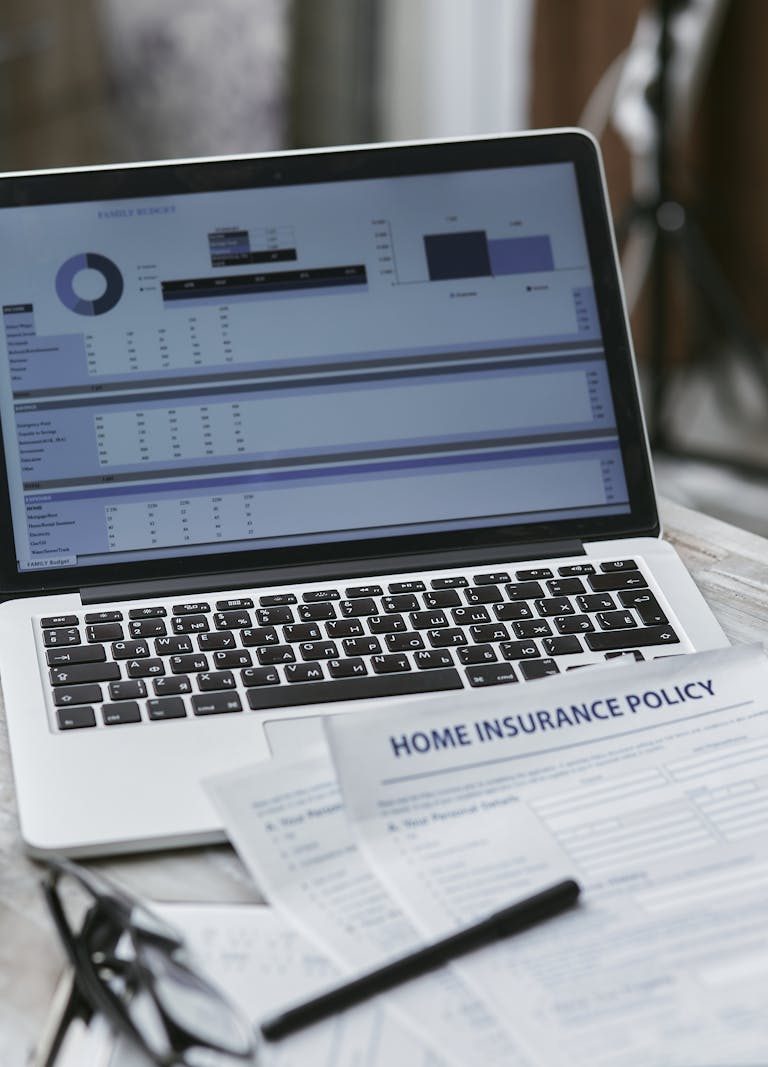 Close-up of home insurance policy papers with a laptop displaying financial analysis.