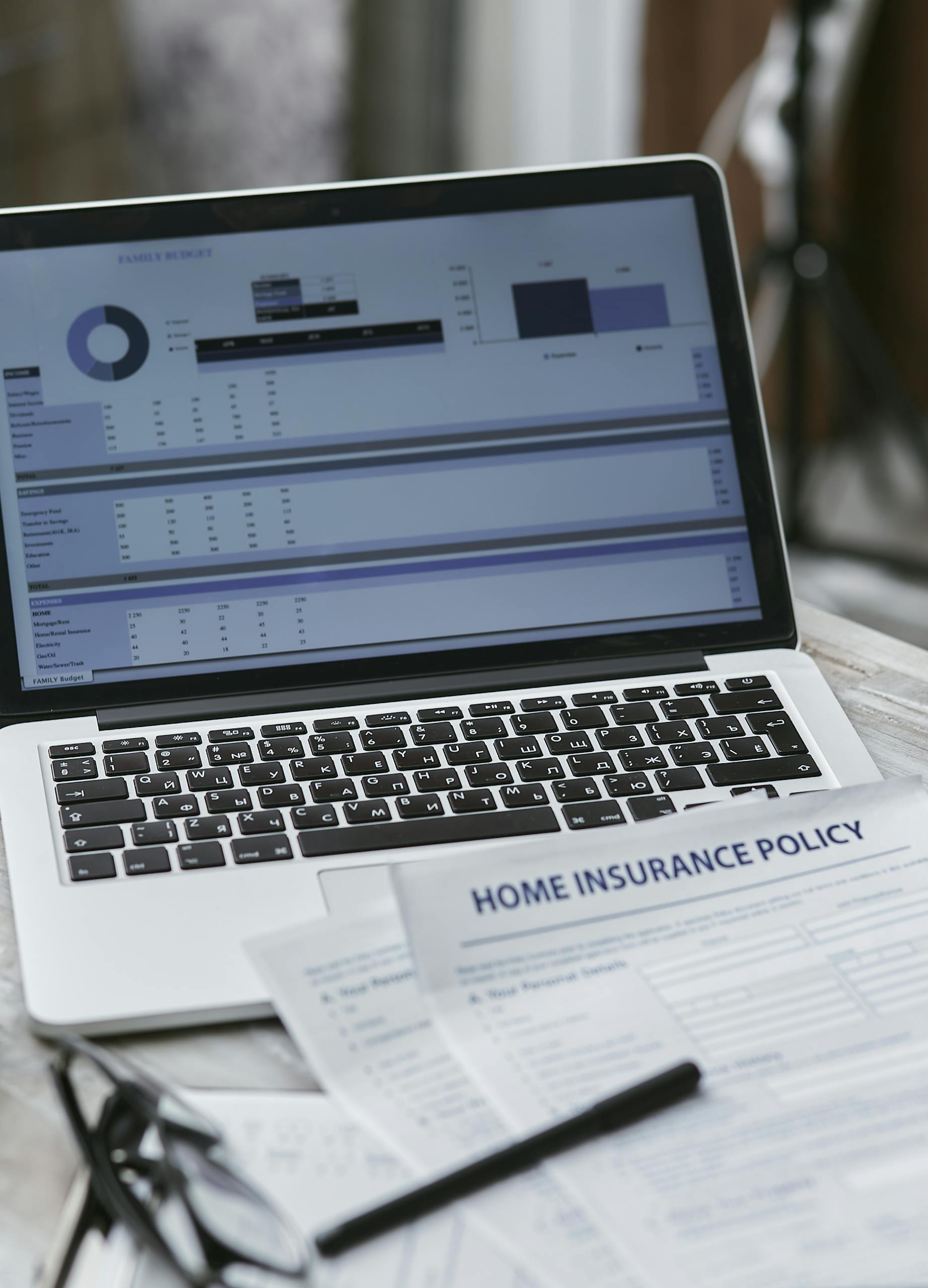 Close-up of home insurance policy papers with a laptop displaying financial analysis.
